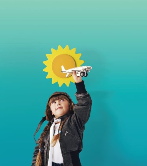 Girl (3-5) wearing hood holding up toy aeroplane